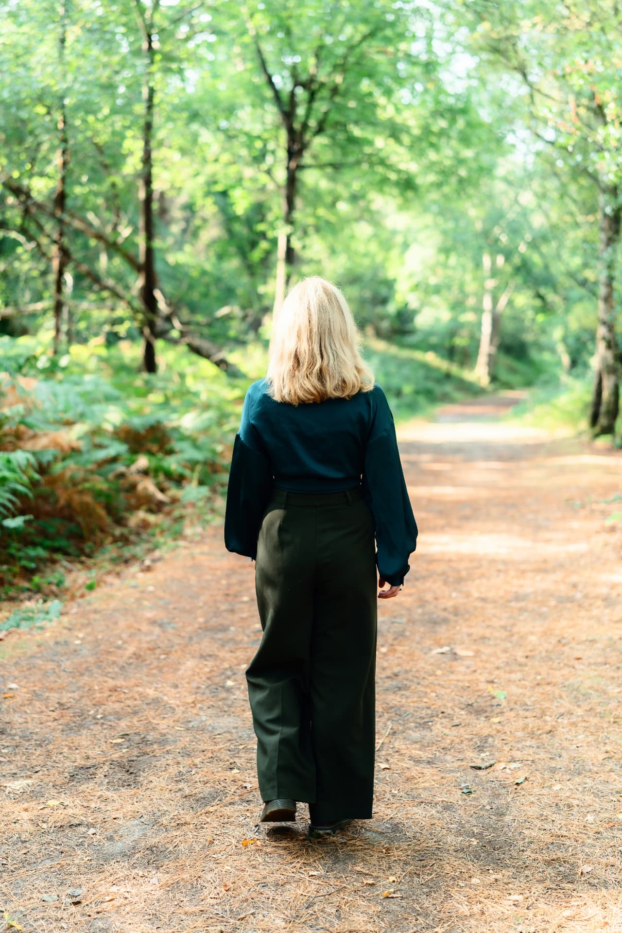 Gemma walking away along a sunlit woodland path