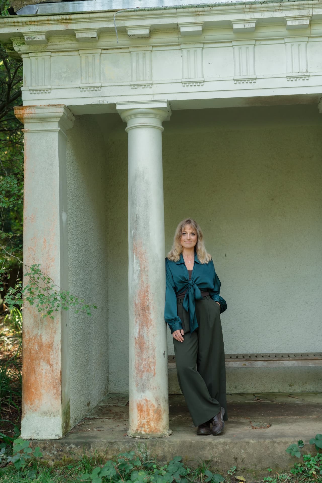 Gemma leaning against a stone column in a woodland garden