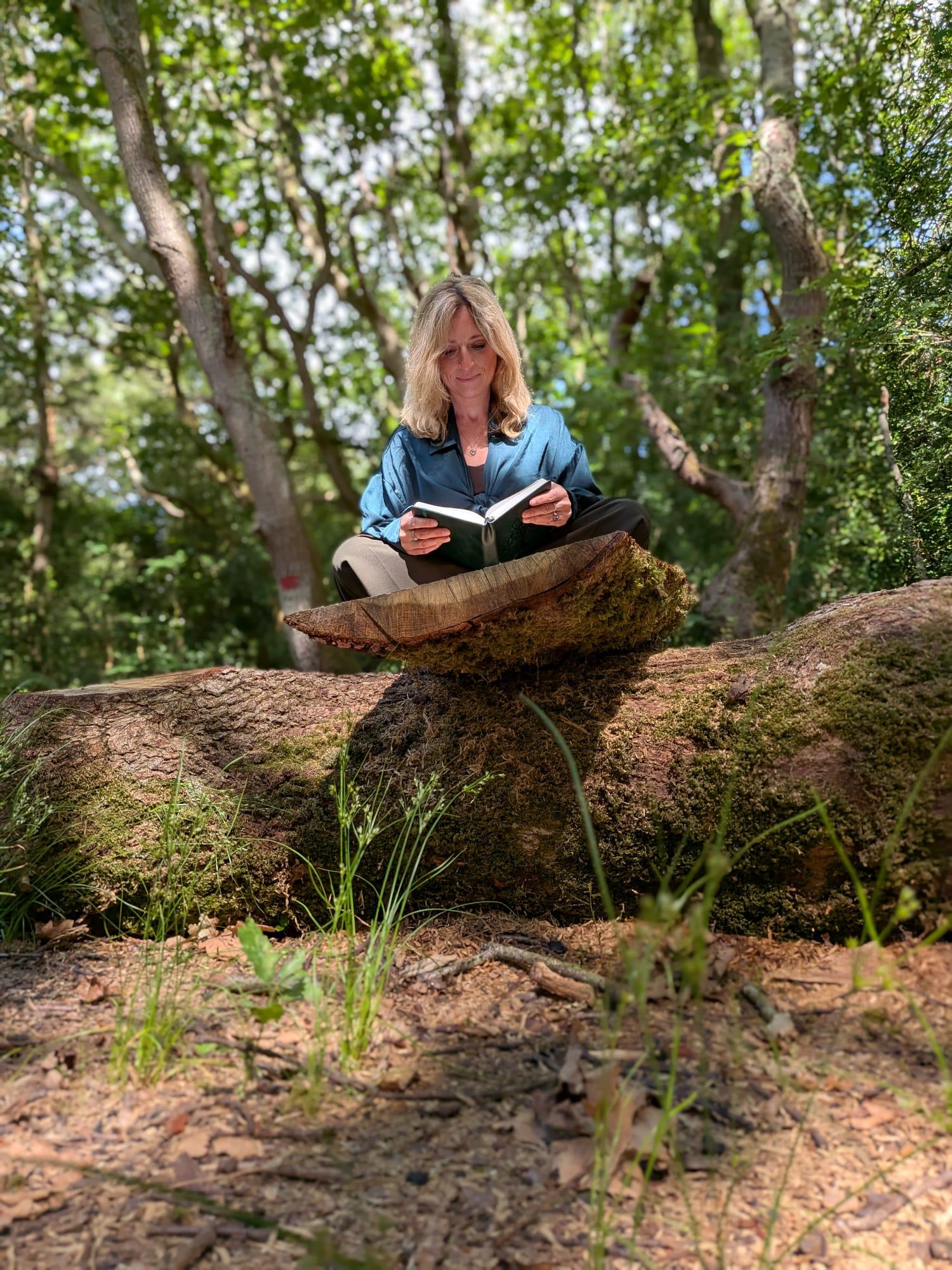 Gemma sitting outdoors with a book, surrounded by trees